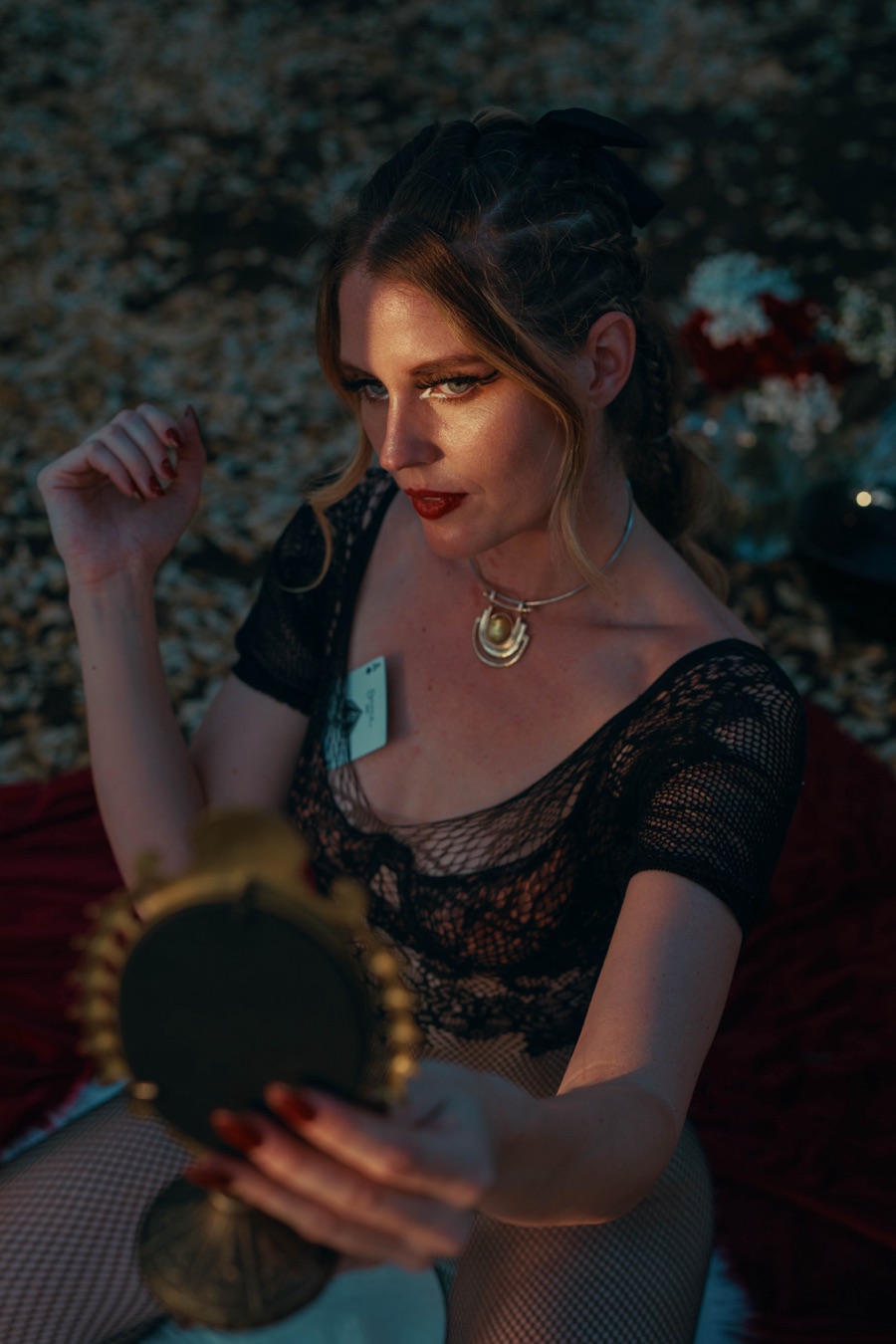 A woman gazing into a golden hand mirror, lit in gold against shadow